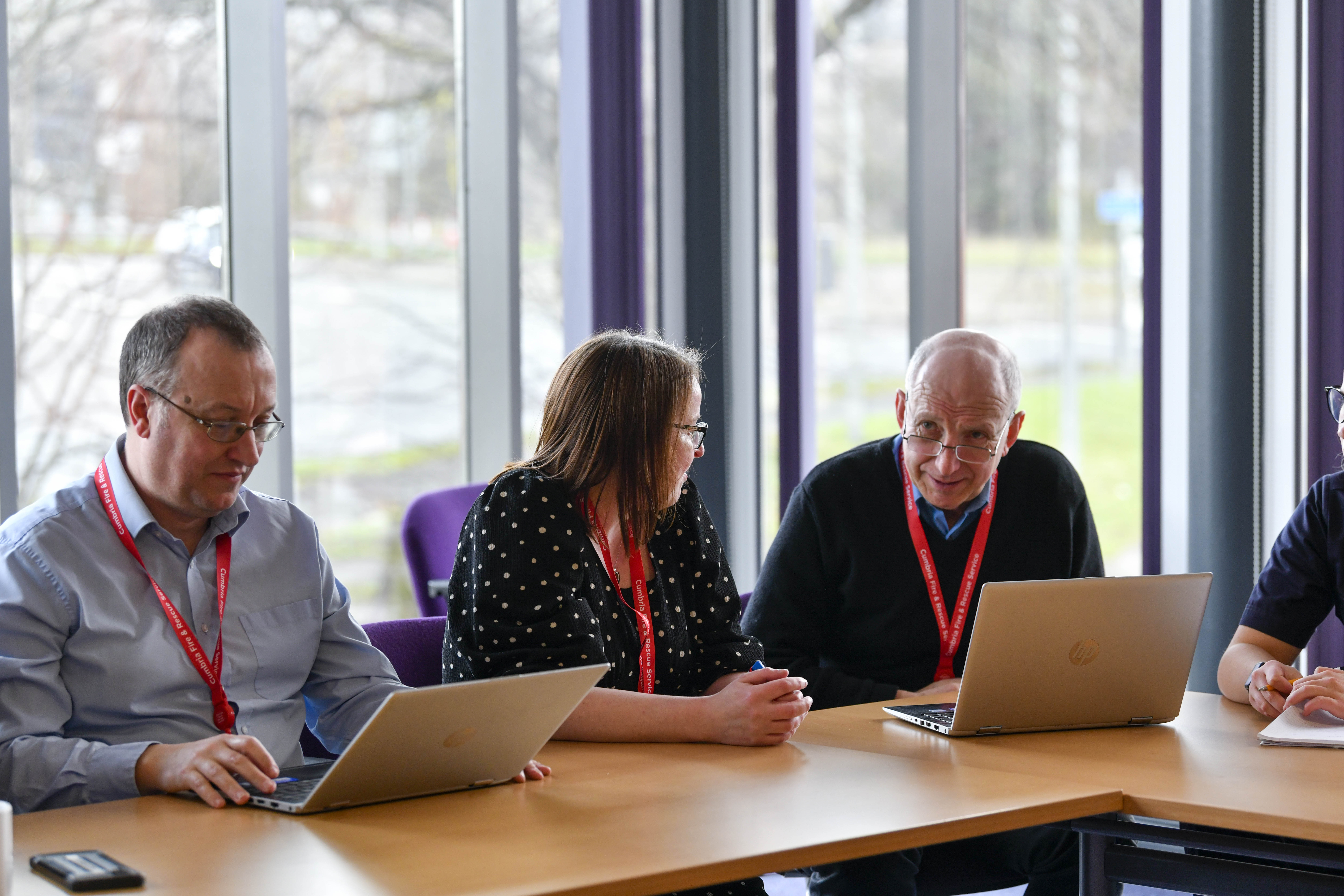 Three members of staff sat in a meeting in smart officewear, with one female presenting employee and two male presenting employees