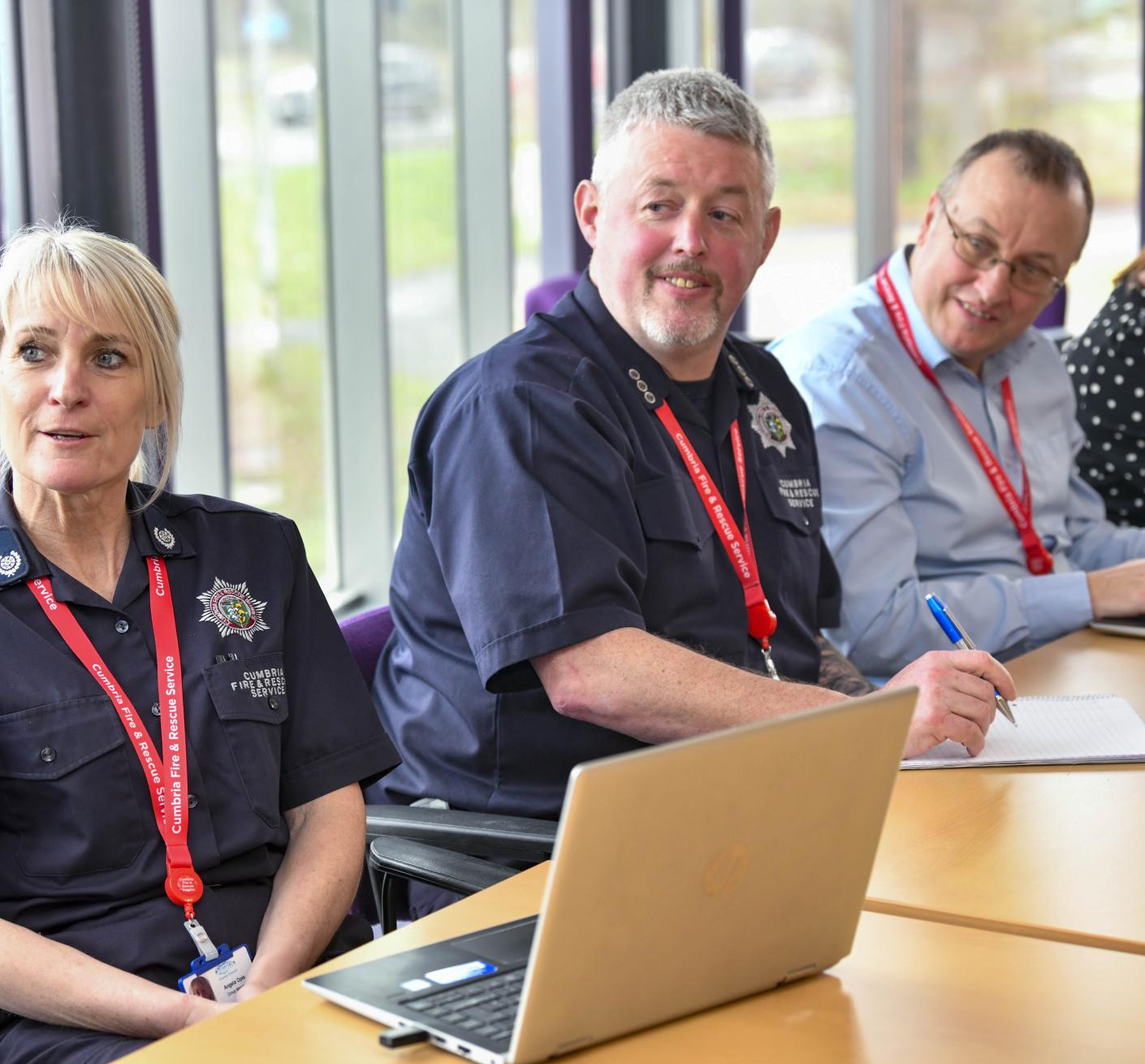 Four members of staff sat in a meeting, some wearing fire uniform and others in smart officewear, with two female presenting employees and two male presenting employees